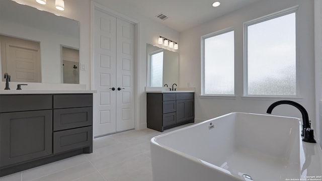 bathroom featuring a freestanding bath, two vanities, a sink, and visible vents