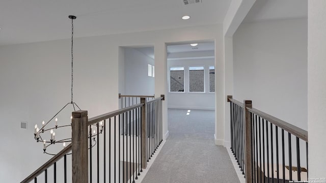 hallway with baseboards, visible vents, an inviting chandelier, an upstairs landing, and carpet floors