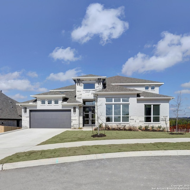 prairie-style house featuring an attached garage, driveway, stone siding, roof with shingles, and a front yard