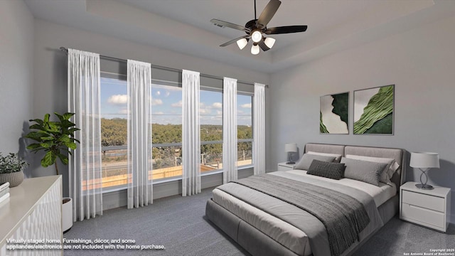 carpeted bedroom with a raised ceiling and a ceiling fan