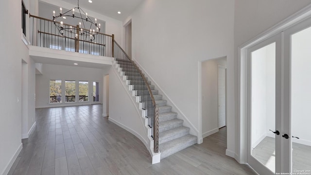 stairs featuring wood-type flooring, a towering ceiling, an inviting chandelier, and french doors