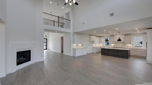 unfurnished living room featuring light wood finished floors, visible vents, a glass covered fireplace, a sink, and baseboards