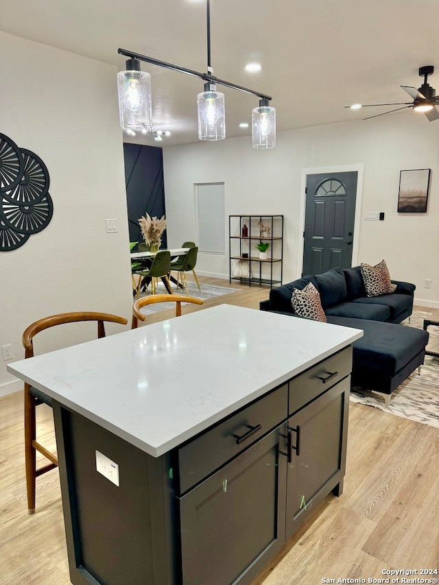 kitchen featuring light wood-type flooring, hanging light fixtures, a kitchen island, light stone countertops, and ceiling fan