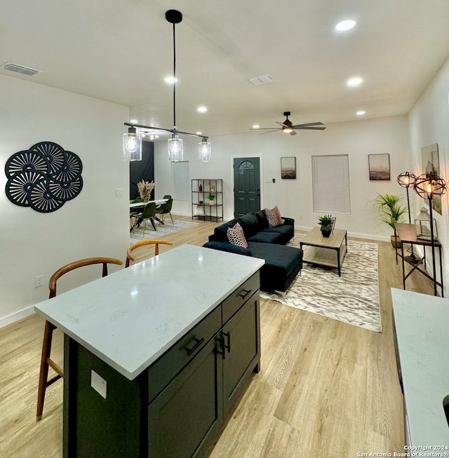 kitchen featuring ceiling fan, a center island, light stone countertops, and light hardwood / wood-style flooring