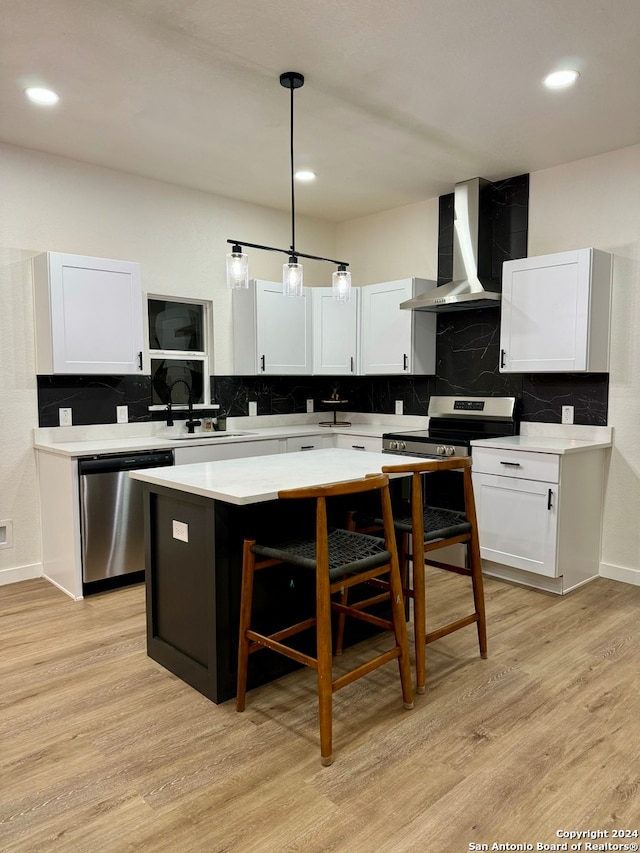 kitchen featuring wall chimney range hood, a kitchen island, stainless steel appliances, and light hardwood / wood-style flooring