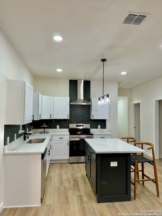 kitchen featuring appliances with stainless steel finishes, a kitchen island, wall chimney exhaust hood, and light hardwood / wood-style flooring