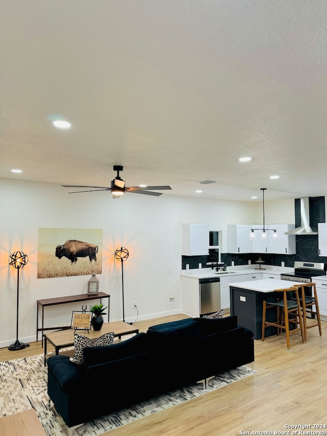 living room with a textured ceiling, ceiling fan, and light wood-type flooring