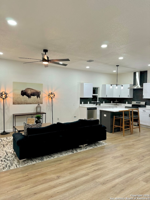 living room with a textured ceiling, ceiling fan, and light wood-type flooring