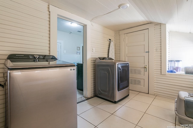 laundry area with light tile patterned floors, wooden walls, and separate washer and dryer