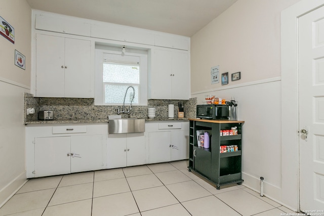 kitchen with light tile patterned floors, light stone countertops, sink, and white cabinets