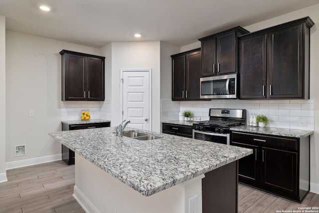 kitchen with light wood-type flooring, appliances with stainless steel finishes, a kitchen island with sink, and sink