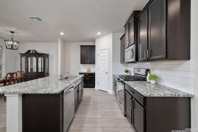 kitchen with stainless steel appliances, an inviting chandelier, decorative backsplash, a center island with sink, and light hardwood / wood-style floors