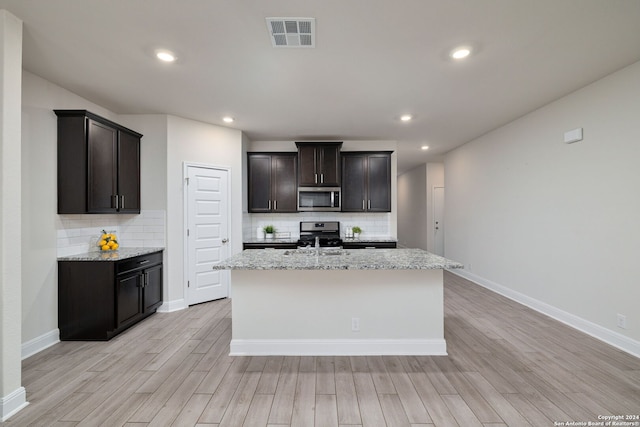 kitchen featuring an island with sink, light wood-type flooring, light stone counters, and appliances with stainless steel finishes