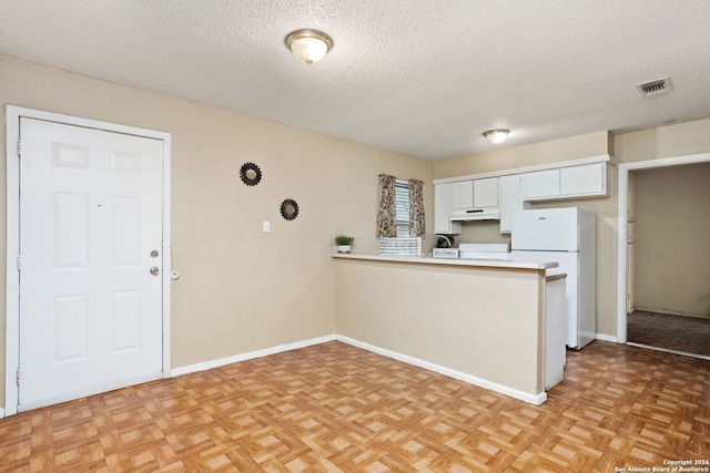 kitchen featuring freestanding refrigerator, a peninsula, light countertops, a textured ceiling, and under cabinet range hood