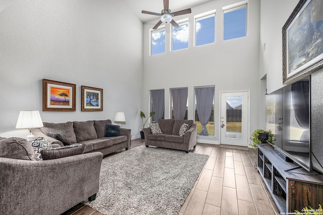 living room with light wood-type flooring, a towering ceiling, a healthy amount of sunlight, and ceiling fan