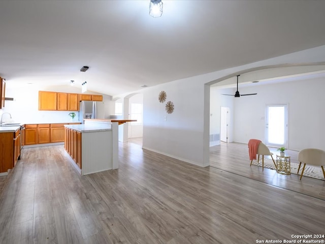 kitchen with hardwood / wood-style flooring, lofted ceiling, stainless steel fridge, ceiling fan, and a kitchen island