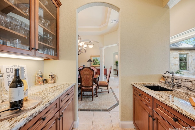 kitchen featuring ornate columns, sink, light stone counters, a notable chandelier, and light tile patterned flooring