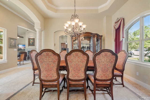 tiled dining room with ceiling fan with notable chandelier, a raised ceiling, ornate columns, and crown molding