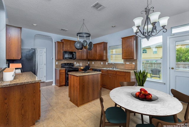 kitchen with a notable chandelier, a kitchen island, a sink, black appliances, and tasteful backsplash