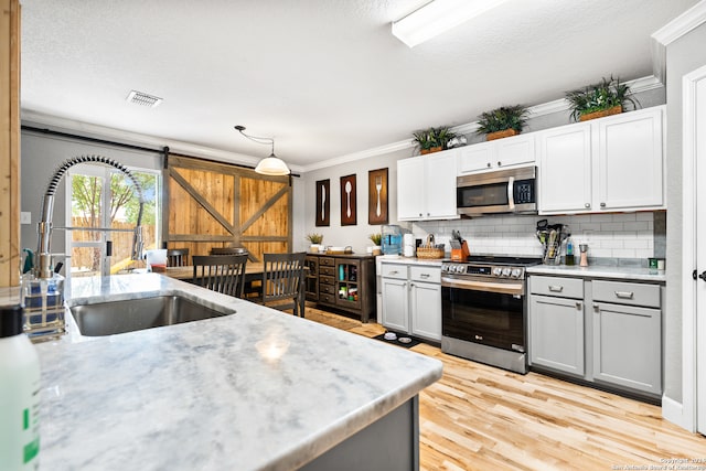 kitchen with appliances with stainless steel finishes, crown molding, sink, decorative backsplash, and light wood-type flooring