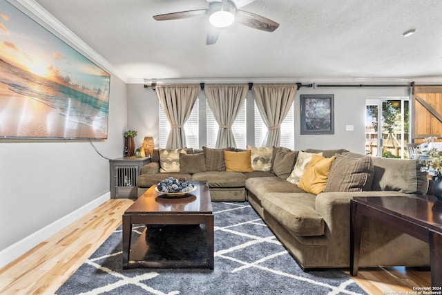 living room with crown molding, a textured ceiling, wood-type flooring, ceiling fan, and a barn door