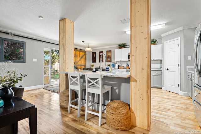 kitchen featuring hanging light fixtures, ornamental molding, white cabinetry, and light hardwood / wood-style flooring