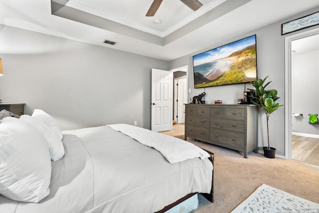 bedroom featuring crown molding, ensuite bath, light colored carpet, a raised ceiling, and ceiling fan