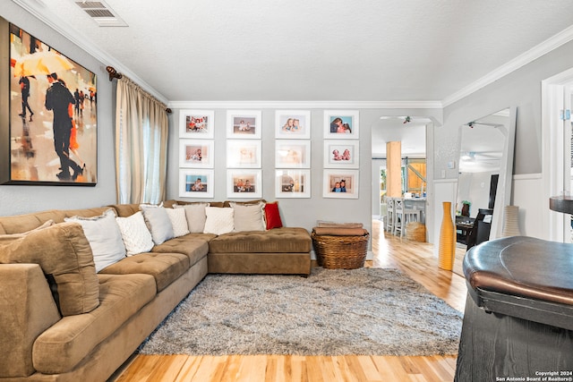 living room with ceiling fan, ornamental molding, a textured ceiling, and light hardwood / wood-style flooring