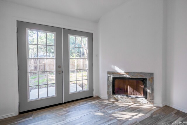 doorway to outside with light hardwood / wood-style floors, vaulted ceiling, french doors, and a fireplace