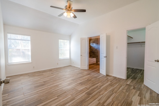 unfurnished bedroom featuring vaulted ceiling, a spacious closet, a closet, light hardwood / wood-style floors, and ceiling fan