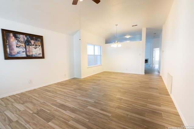 unfurnished room with ceiling fan with notable chandelier, light hardwood / wood-style floors, and vaulted ceiling