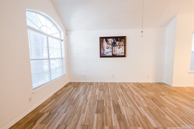 unfurnished room featuring lofted ceiling, a wealth of natural light, and hardwood / wood-style flooring