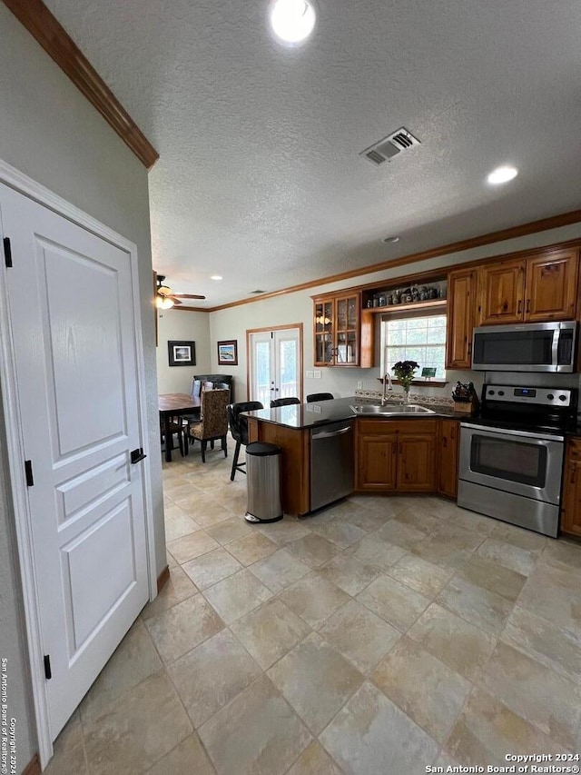 kitchen with appliances with stainless steel finishes, sink, ornamental molding, and a textured ceiling