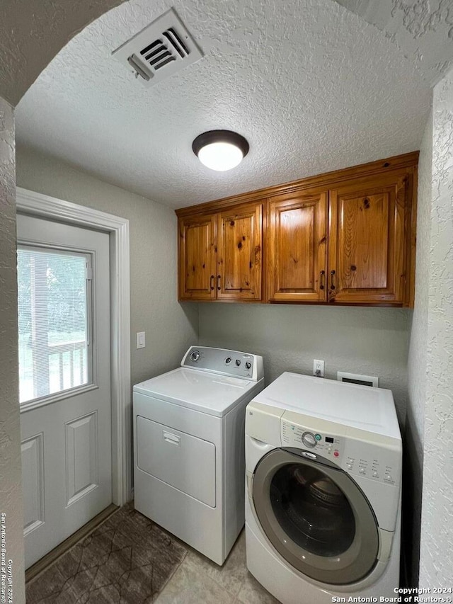 clothes washing area featuring cabinets, a textured ceiling, and washer and dryer