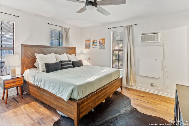 bedroom with ceiling fan, a wall mounted air conditioner, and light hardwood / wood-style floors