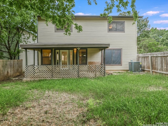 back of house featuring covered porch, a lawn, and central air condition unit