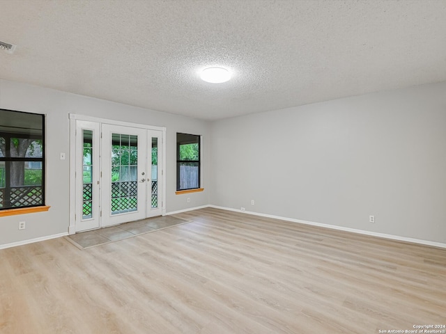 empty room with french doors, a textured ceiling, and light hardwood / wood-style floors