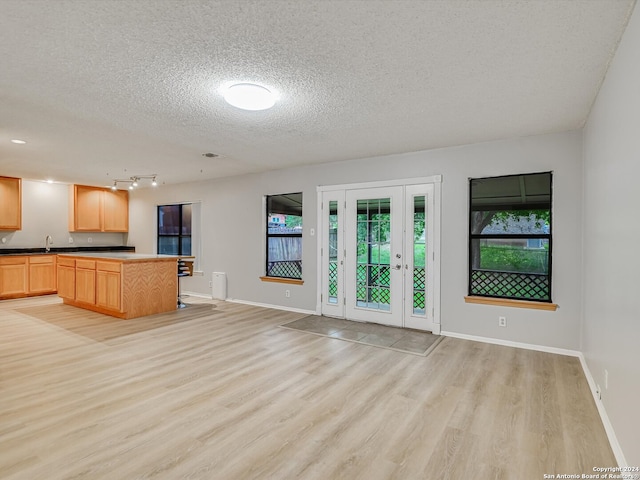 unfurnished living room with light wood-type flooring, sink, and a textured ceiling