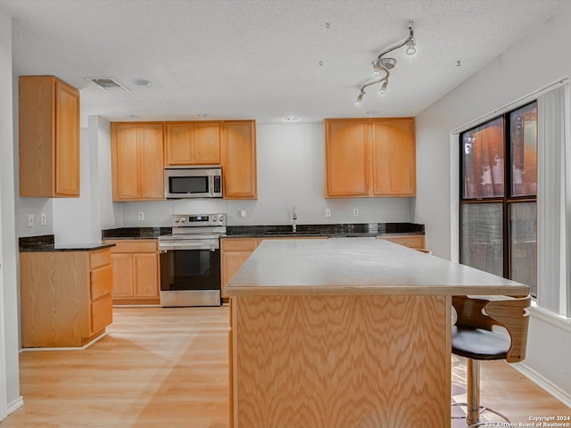 kitchen featuring a center island, appliances with stainless steel finishes, light hardwood / wood-style floors, sink, and a textured ceiling