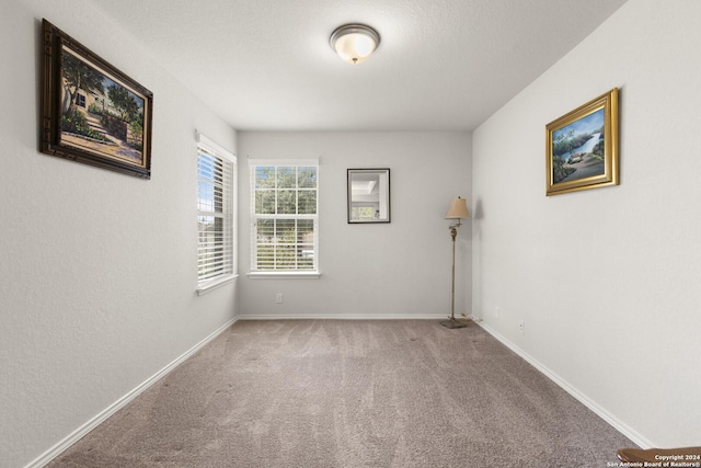 empty room featuring a textured ceiling, carpet, and baseboards