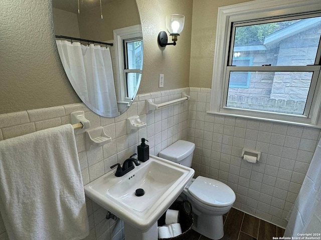 bathroom with toilet, backsplash, wood-type flooring, sink, and tile walls