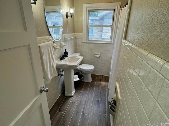 bathroom featuring a textured wall, toilet, a wainscoted wall, wood tiled floor, and tile walls