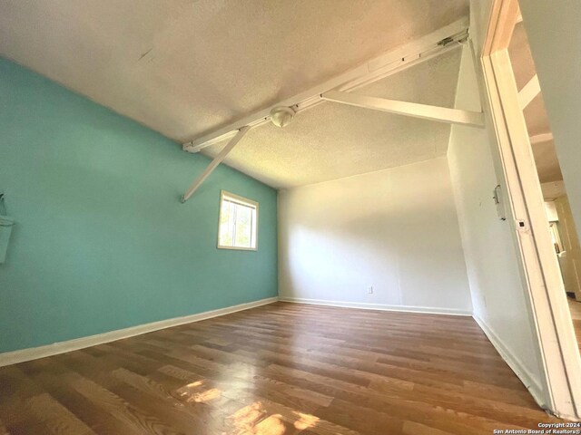 additional living space featuring lofted ceiling, dark hardwood / wood-style flooring, and a textured ceiling