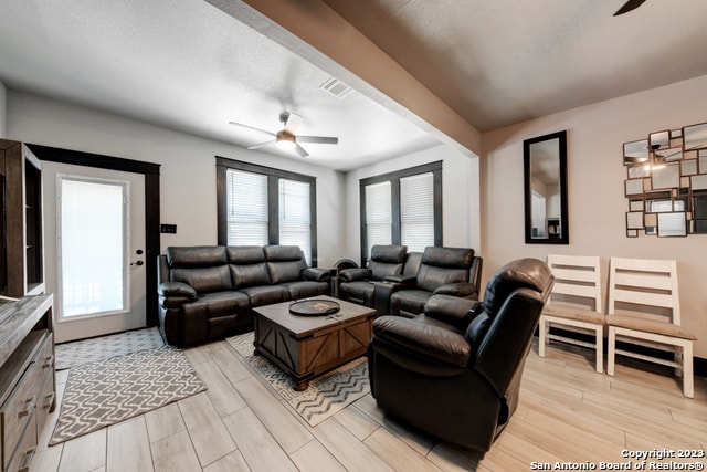 living room with a textured ceiling, ceiling fan, and light hardwood / wood-style floors