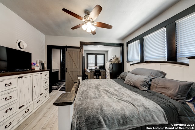 bedroom with light hardwood / wood-style flooring, ceiling fan, and a barn door