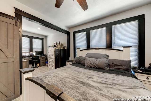 bedroom featuring light wood-type flooring, ceiling fan, and a barn door