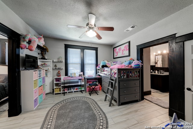 bedroom with light wood-type flooring, a textured ceiling, connected bathroom, and ceiling fan
