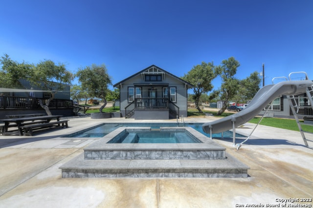 view of pool featuring a water slide and an in ground hot tub