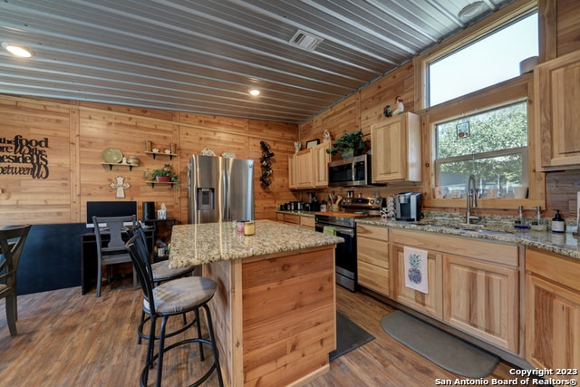 kitchen featuring wood walls, light stone countertops, hardwood / wood-style floors, a center island, and stainless steel appliances