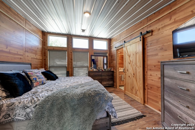 bedroom with a barn door, hardwood / wood-style floors, multiple windows, and wooden walls